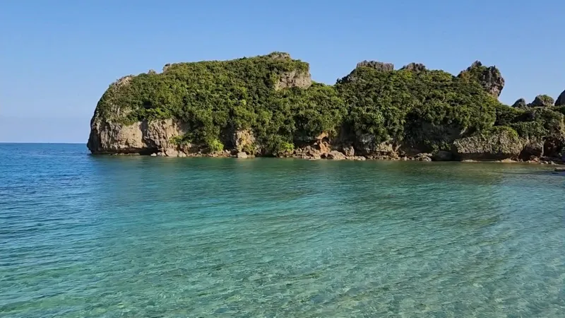 Aguas turquesas cristalinas con colinas verdes al fondo en Hamahigajima