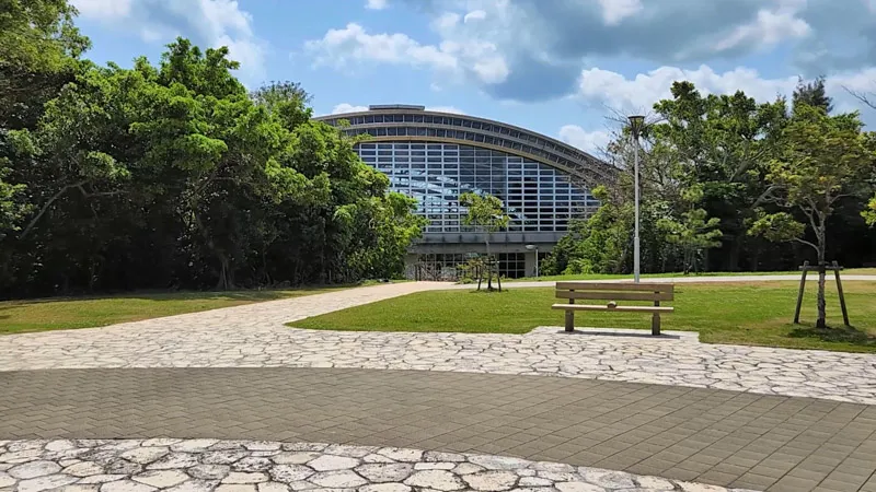 Gran sala acristalada rodeada de vegetación en el Parque Deportivo de Kitanakagusuku Okinawa